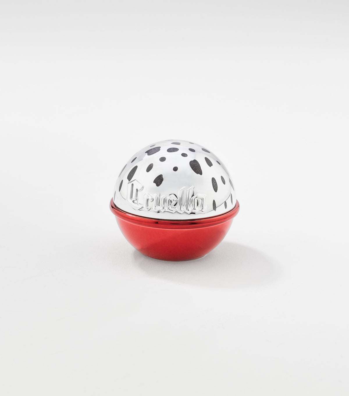 A round lip balm container with a glossy red base and a silver dome lid decorated with black spots and "Cruella" lettering.