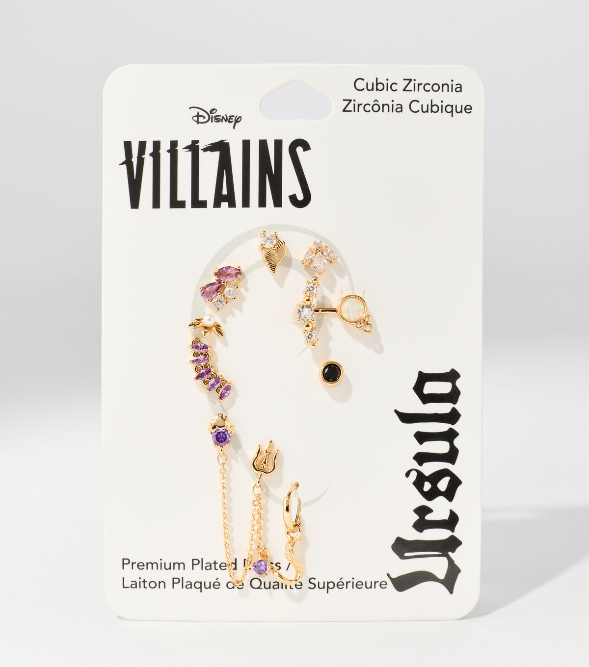 Gold-tone earrings with purple and clear crystals, a chain, and a trident charm are displayed on a white Disney Villains Ursula card.