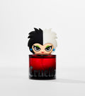 A red glass perfume bottle with "Cruella" in gothic lettering is topped by a cartoon head with half black, half white hair.