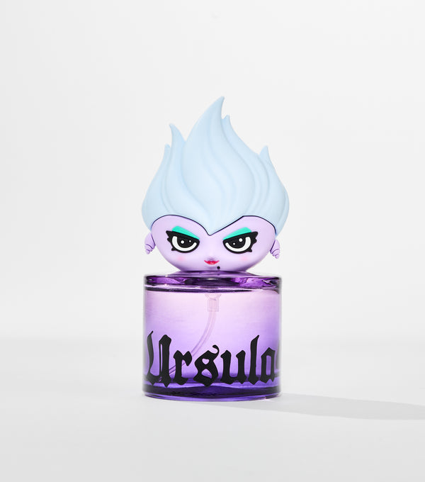 A round purple glass perfume bottle with black gothic lettering, topped by a cartoon figure with pale blue flame-like hair.