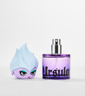 A purple glass perfume bottle with black gothic lettering and silver spray nozzle sits beside its cartoon character cap with pale blue hair.