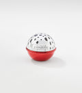 A round lip balm container with a glossy red base and a silver dome lid decorated with black spots and "Cruella" lettering.