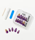 Purple almond-shaped press-on nails with gold drip tips and charms sit in a clear case beside nail glue, a file, and a cuticle stick.