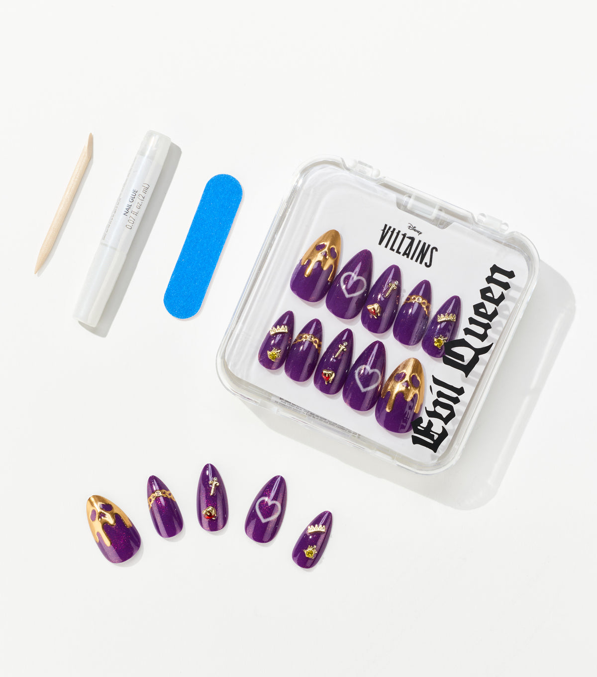 Purple almond-shaped press-on nails with gold drip tips and charms sit in a clear case beside nail glue, a file, and a cuticle stick.