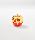 A glossy red apple-shaped container topped with dripping gold coating that forms a skull face with cutout eyes and nose.