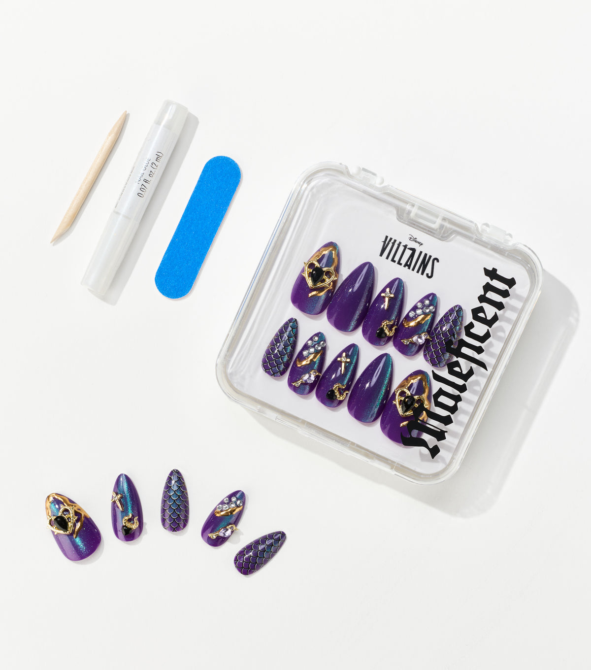Purple almond-shaped press-on nails with gold charms and scale patterns sit in a clear case beside a nail file, glue, and stick.