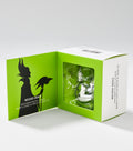 An open green and white gift box shows a silver lip balm in a clear window beside a black horned silhouette.