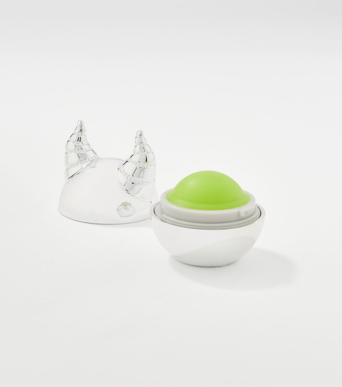 An open spherical lip balm with a green dome inside a white base, beside a silver horned lid.