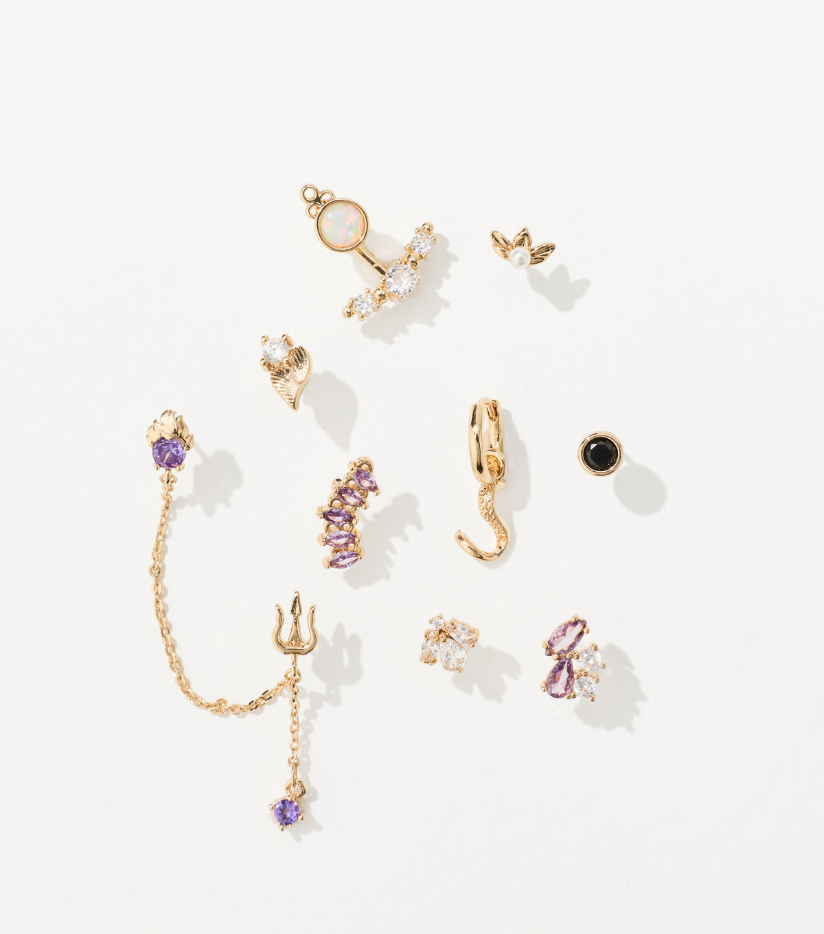 Ten gold-tone earrings with purple, clear and black gems, including a trident chain drop and a hoop with a tentacle charm.