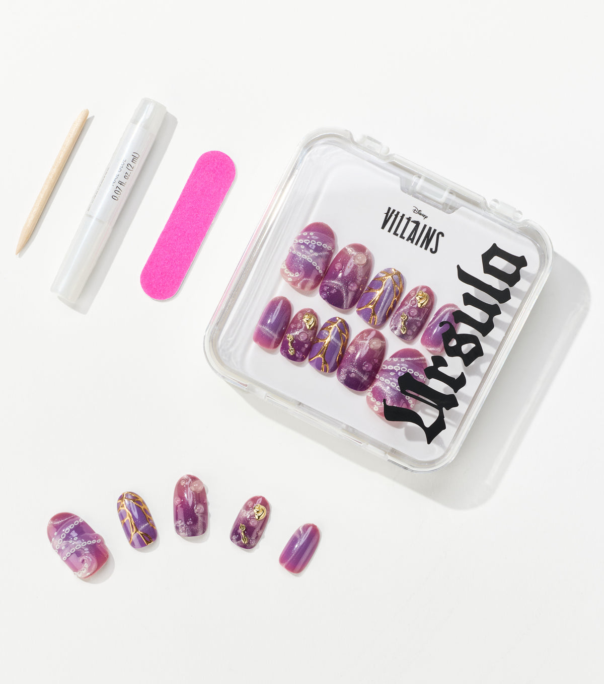 Purple press-on nails with gold accents in a clear Disney Villains Ursula case, beside a pink nail file, glue pen, and cuticle stick.