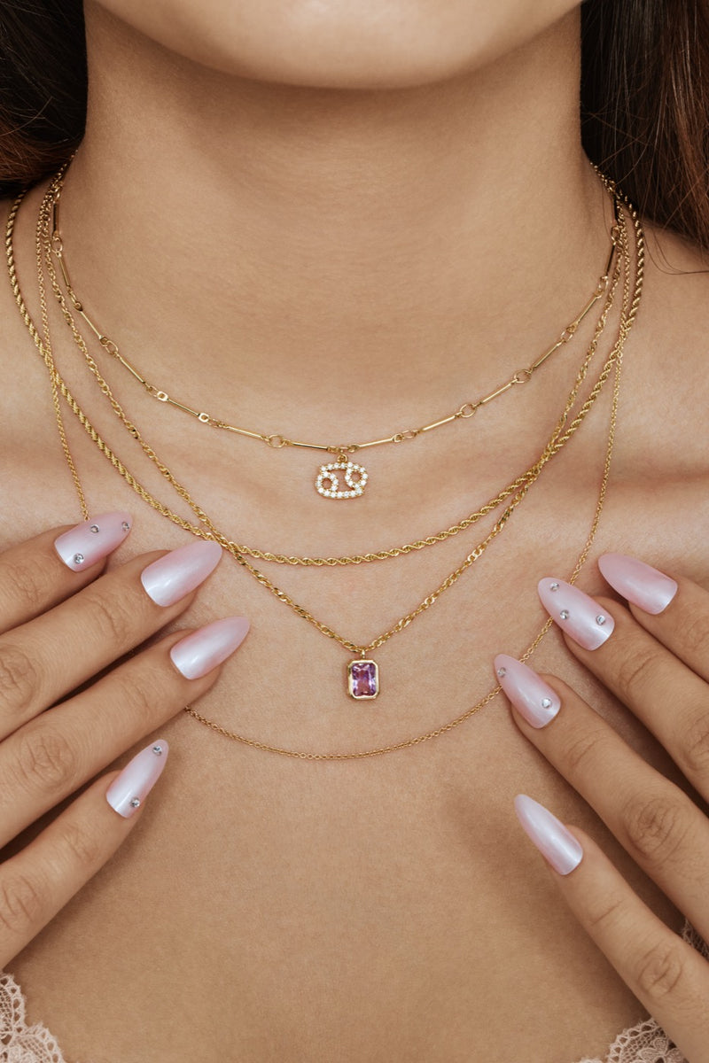 Layered gold necklaces with a zodiac charm and a pink gemstone pendant